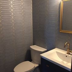 a white toilet sitting next to a sink in a bathroom under a mirror with a gold framed mirror above it