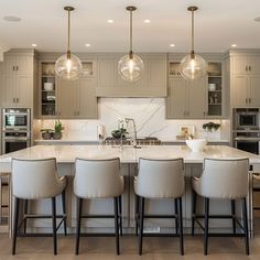 a large kitchen with an island and four bar stools in front of the sink