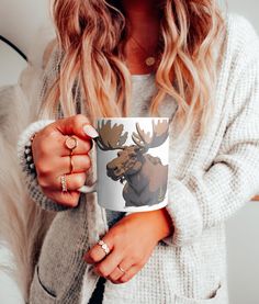 a woman is holding a coffee mug with a moose on it and she has her hands in the cup