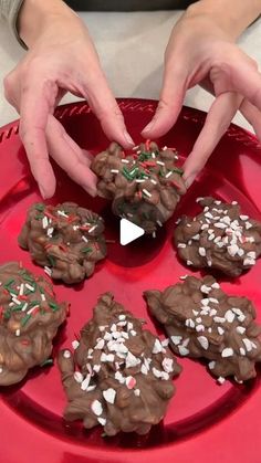 someone decorating chocolate cookies on a red plate with white and green sprinkles