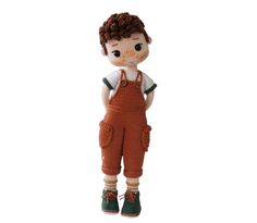 a crocheted doll with brown overalls and green shoes is standing in front of a white background