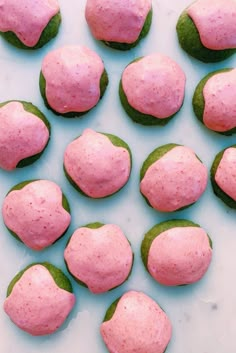 there are many pink and green donuts on the table together, with leaves around them