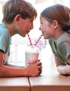 two young children sitting at a table drinking milkshakes