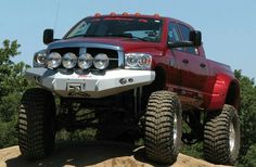 a large red truck driving on top of a dirt hill with trees in the background