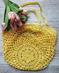 a yellow crocheted bag with flowers in it sitting on a wooden table next to a pink tulip