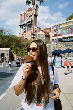 a woman with long brown hair eating a piece of chocolate in front of an amusement park