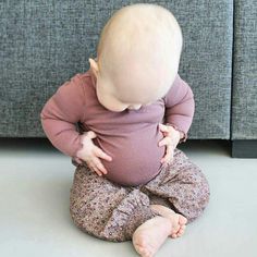 a baby sitting on the floor in front of a couch looking down at her feet