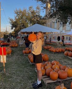 a woman holding a pumpkin in front of a large group of pumpkins on display