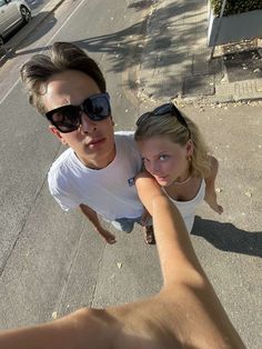 a young man and woman taking a selfie on the street with their hands in each other's pockets