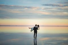 a man carrying a woman on his back walking across a lake at sunset with the sun setting