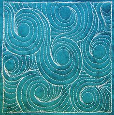 a blue quilt with white stitching and swirls in the center, on top of a