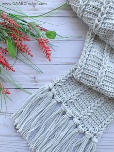 a crocheted scarf with red flowers and greenery next to it on a white wooden surface