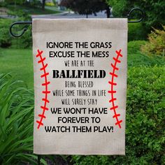 a baseball themed garden flag hanging from a metal pole in front of some bushes and trees