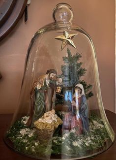 a nativity scene under a glass dome on a wooden table with christmas decorations around it