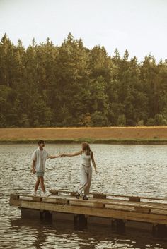 two people walking across a wooden dock over water with trees in the backgroud