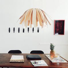 a wooden table topped with a pineapple next to black chairs and a lamp hanging from the ceiling