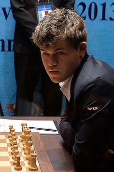 a man sitting at a table with chess pieces in front of him and people behind him