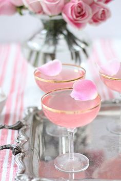 two pink martinis with rose petals in them on a silver tray next to flowers