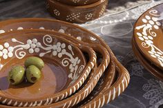 some brown and white bowls with olives in them sitting on a tablecloth covered table