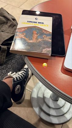 someone is sitting at a table with a book on top of their feet and an ipad in front of them