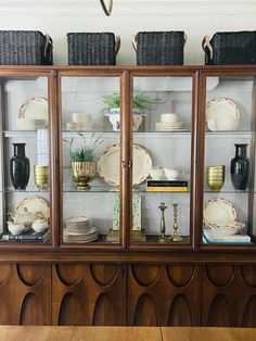 an old china cabinet with wicker baskets on top and plates in the glass doors