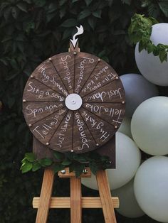 a wooden wheel with writing on it sitting in front of some white and gray balloons