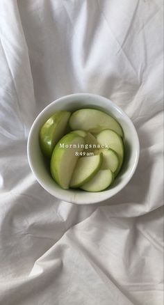 a white bowl filled with sliced apples on top of a bed covered in white sheets