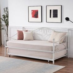 a white daybed sitting on top of a hard wood floor next to two framed pictures