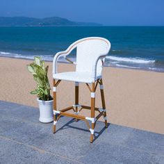 a white chair sitting on top of a cement floor next to the ocean with a potted plant in front of it