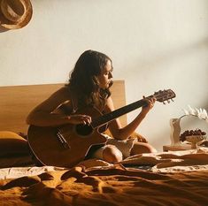 a woman sitting on top of a bed holding a guitar