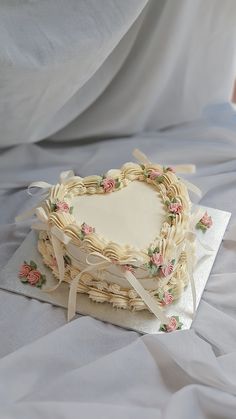 a heart shaped cake on top of a white cloth covered table with ribbon and flowers