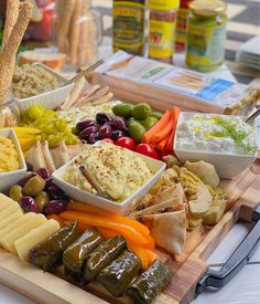 an assortment of food on a wooden platter with cheese, crackers and olives