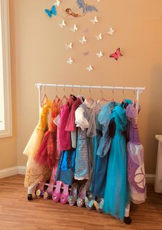 a rack full of children's clothes with butterflies on the wall behind it and a window in the background