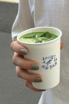 a woman holding a cup of green tea with leaves in it and writing on the side