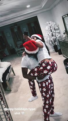 two people dressed in christmas pajamas and santa hats taking a selfie with a cell phone