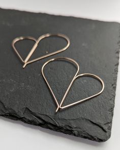 Spread a little love and happiness with the newly updated pull-through heart hoop earrings. These hearts are full of curves, overflowing with love, devoted to accentuate your look. The asymmetrical wire earrings embody a sleek heart motif silhouette and the airy design gracefully shines with elegance. Earring size: petite: 1 1/8" L x 3/4" W (28.6mm x 19mm) tall: 1 1/2” L x 1 1/8” W (38.1mm x 28.6mm) xtall: 2" L x 1 7/8" W NEW SIZE Color options: polished silver charcoal silver yellow gold fill r Minimalist Hoop Earrings With Heart Charm, Minimalist Small Hoop Heart Earrings, Minimalist Dangle Heart Earrings, Minimalist Dangle Hoop Earrings For Valentine's Day, Minimalist Heart Jewelry With Ear Wire, Minimalist Open Heart Hoop Earrings With Heart Charm, Modern Heart-shaped Hoop Earrings For Gift, Modern Heart-shaped Hoop Earrings Gift, Minimalist Hypoallergenic Hoop Earrings For Valentine's Day