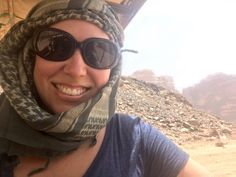 a woman wearing sunglasses and a scarf around her head in the desert with mountains in the background