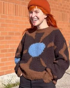 a woman standing in front of a brick wall wearing a sweater with blue circles on it