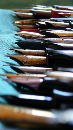 many pens are lined up on a blue table cloth with green edges and black tips