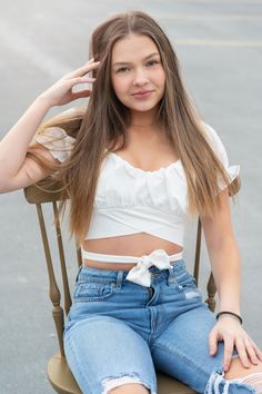 a young woman sitting in a chair with her legs crossed and wearing ripped denims