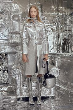 a woman standing in front of a silver wall with a kettle on it's feet