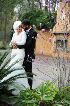 a bride and groom standing next to each other in front of some trees with purple flowers