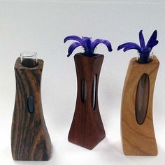 three wooden vases with blue flowers in them on a white surface, one is made out of wood