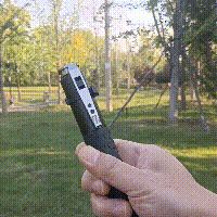 a hand holding a remote control in front of a grassy area with trees and grass