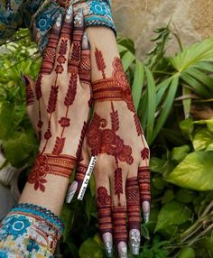 two hands with henna designs on them and green plants in the backgroud