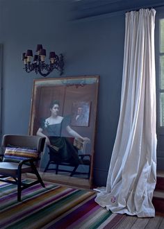 a woman sitting in a chair next to a painting on the wall near a window