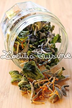 a glass jar filled with dried herbs on top of a wooden table