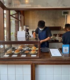 two people standing behind a counter with pastries on it