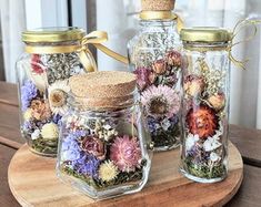 three glass jars filled with flowers sitting on top of a wooden table next to each other