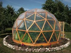 a large glass dome sitting on top of a lush green field next to rocks and trees